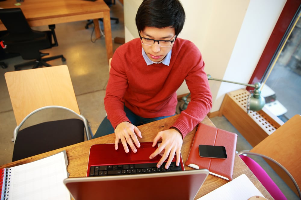 Young asian man in glasses working on laptop in office